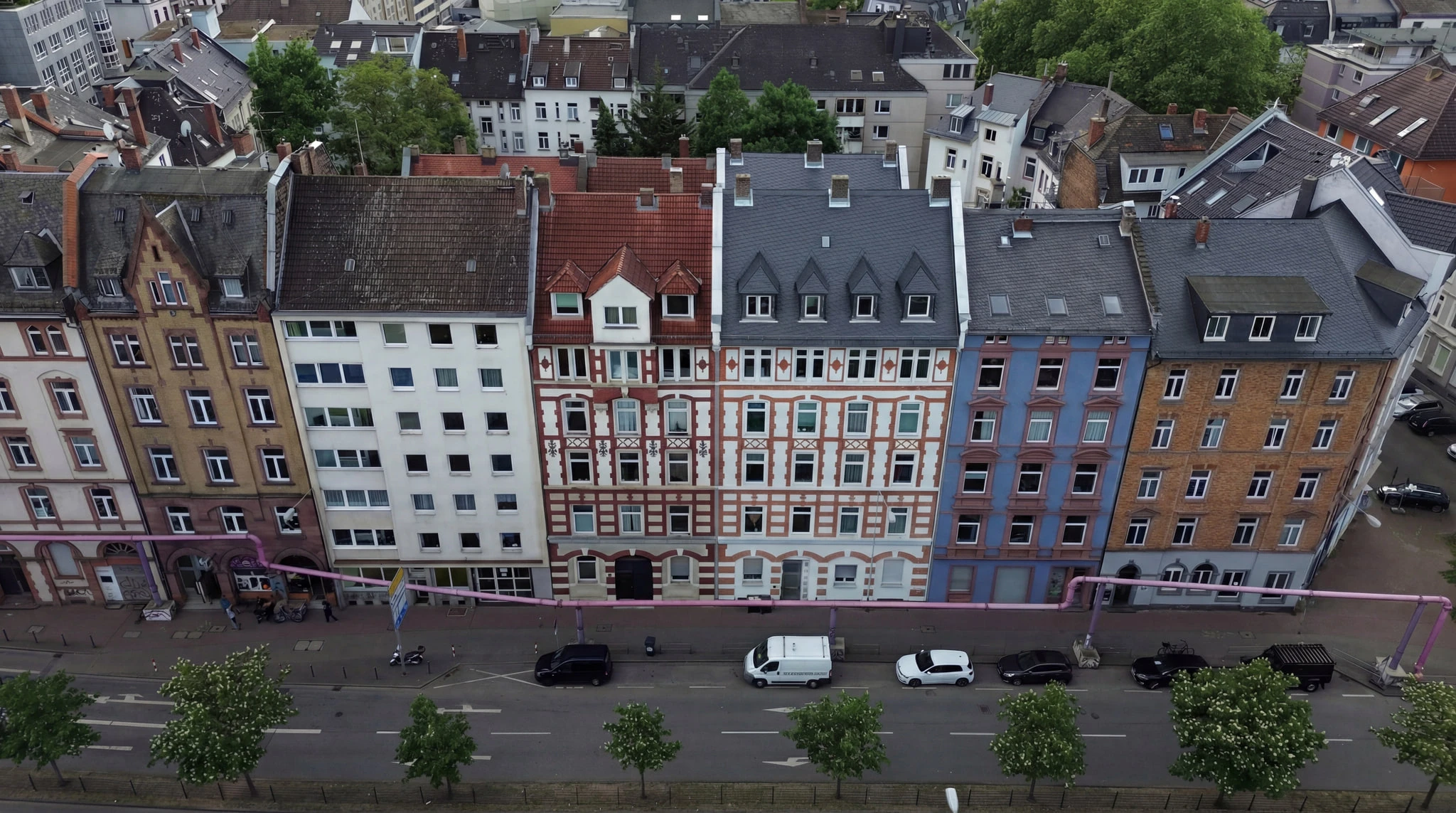Das Projekt HERITAGE 27 aus der Luft über der Straße: eine Reihe farbig verputzter Gründerzeithäuser mit unterschiedlich gedeckten Dächern, davor eine Allee und parkende Autos.