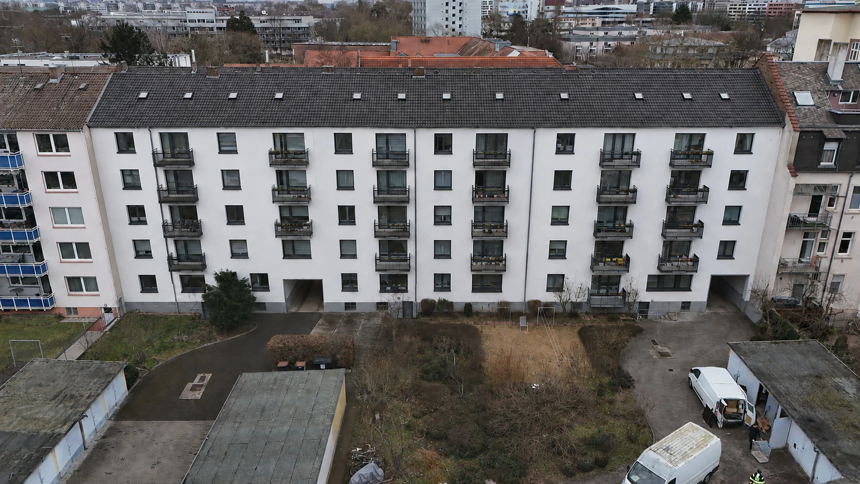 Die Rückseite des Projekts ENSEMBLE 27 aus der Luft: die durchgehende weiße Fassade mit Balkonreihen, davor die Hoffläche mit Zufahrt und Bäumen.