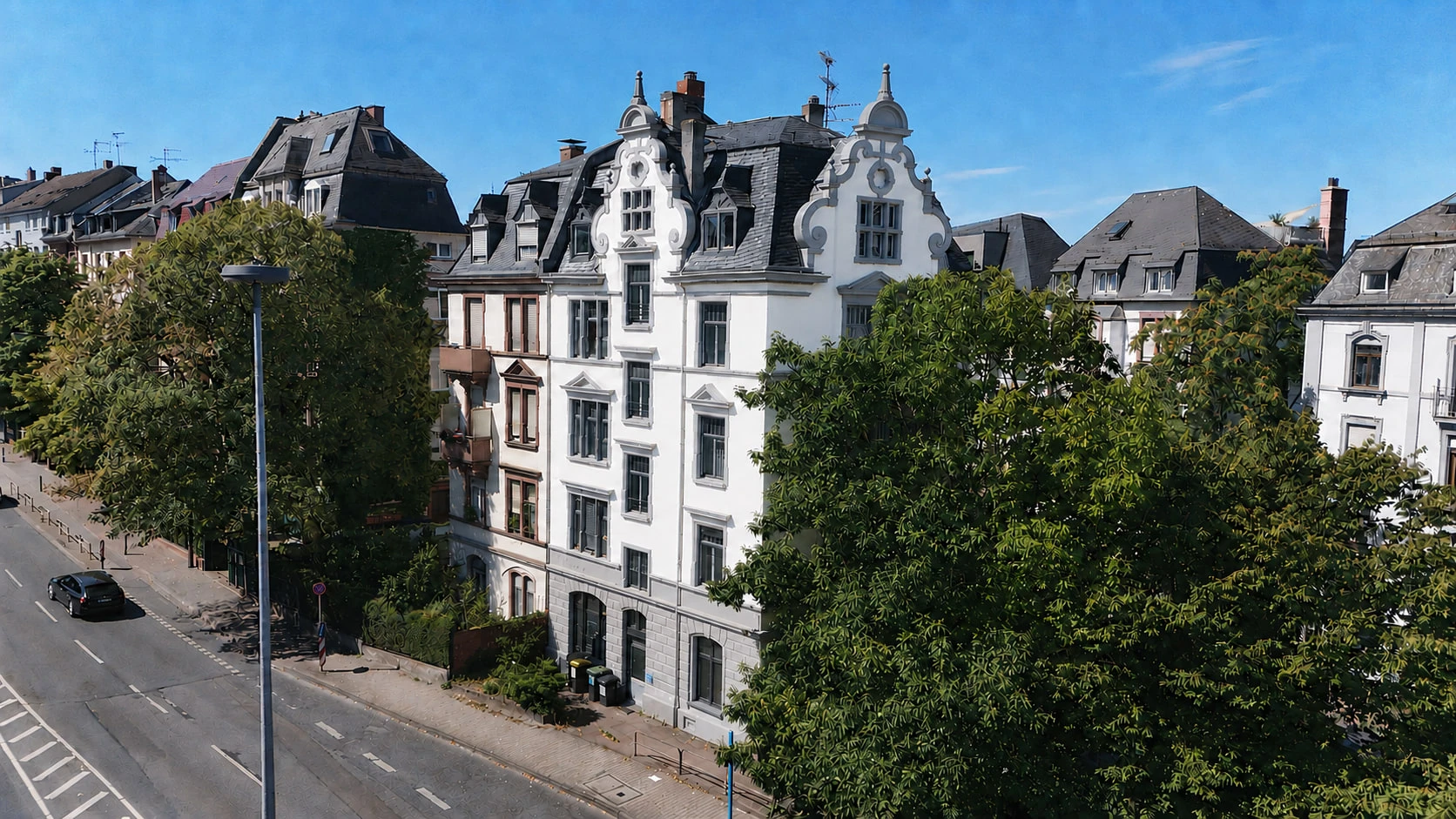Das Projekt CROWN 78 aus der Luft von der anderen Straßenseite: die weiße Fassade mit Ziergiebel in der Häuserzeile, davor die Straße mit Laternenmast und Bäumen.