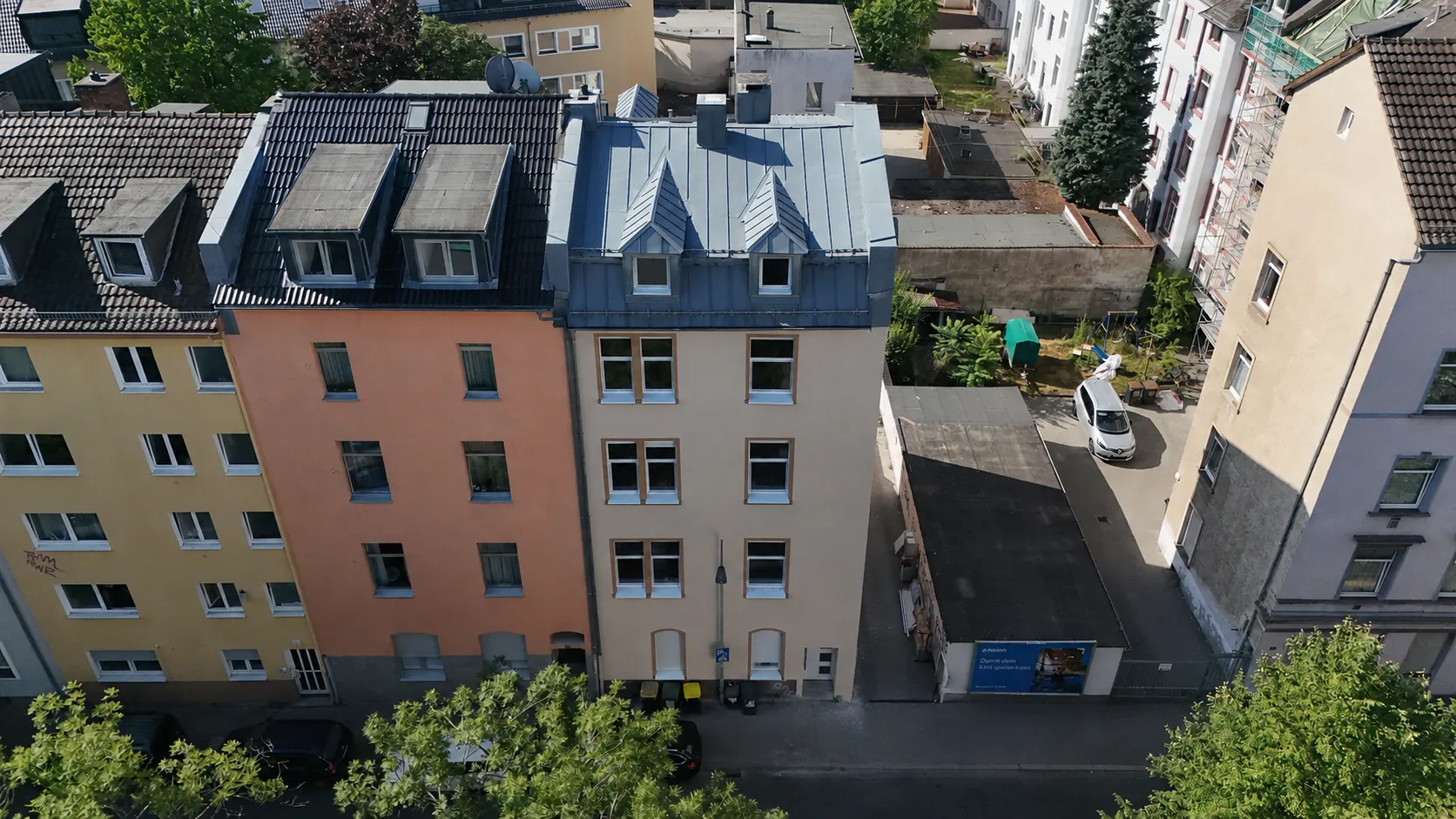 Luftaufnahme des Projekts WEST 27: ein sandfarbener Altbau mit blaugrau gedecktem Mansarddach in der geschlossenen Häuserzeile, dahinter die Hinterhöfe und Dächer des Viertels.