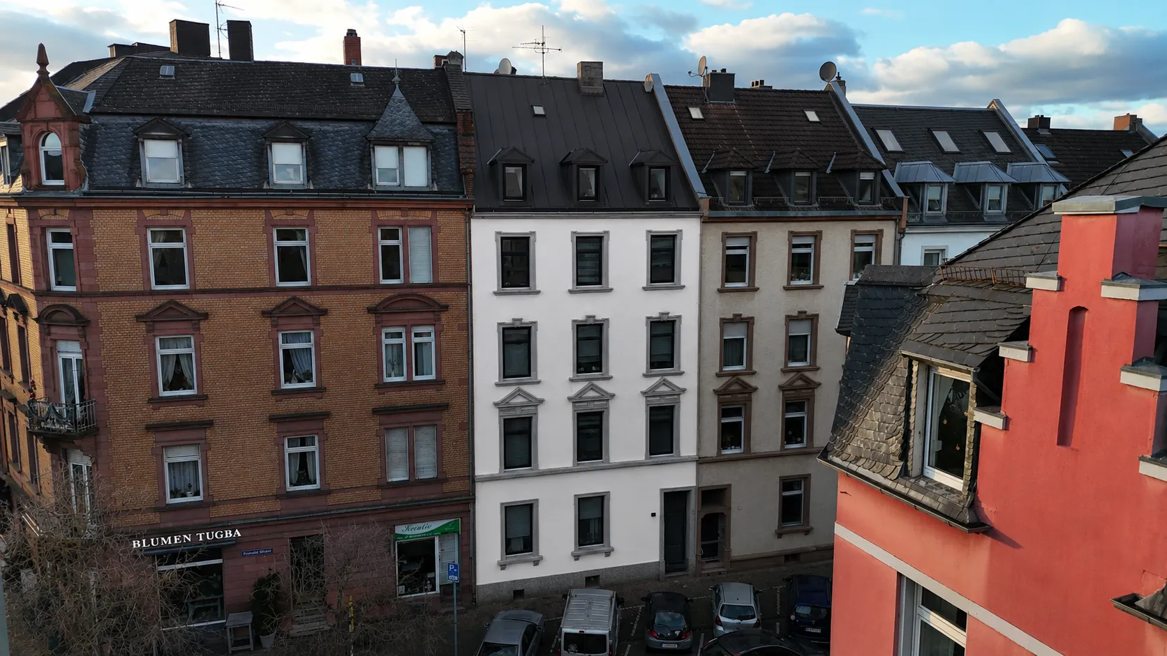 Luftaufnahme des Projekts N°36: ein weiß verputzter Altbau mit dunklem Dach zwischen den farbig verputzten Nachbarhäusern der Straßenzeile, im Erdgeschoss ein Ladenlokal.