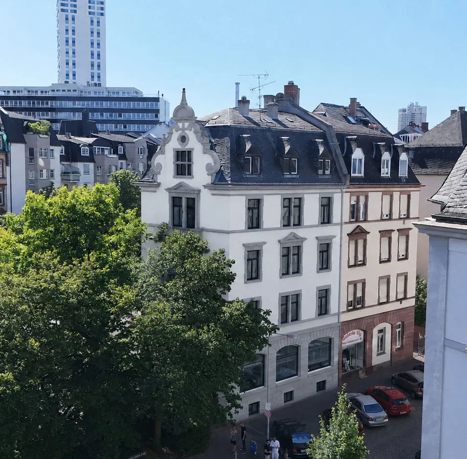Das Projekt CROWN 78 aus der Luft über der Kreuzung: der helle Gründerzeitbau mit Ziergiebel zwischen den Nachbarhäusern, davor Baumkronen und die Straßenzüge des Viertels.
